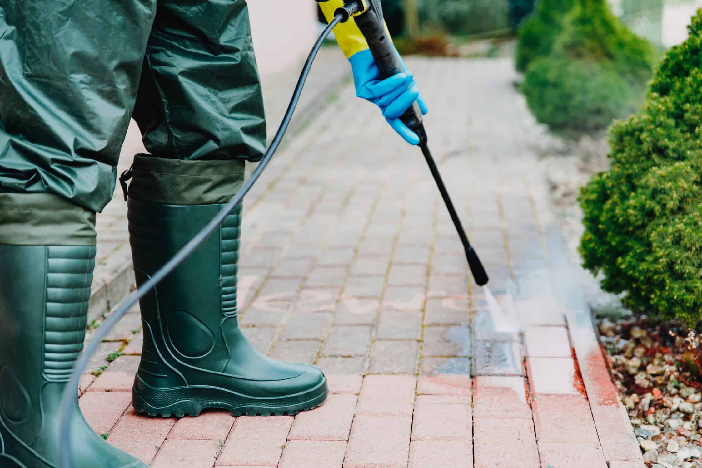 Man cleaning red, conrete pavement block using high pressure water cleaner. Paving cleaning concept