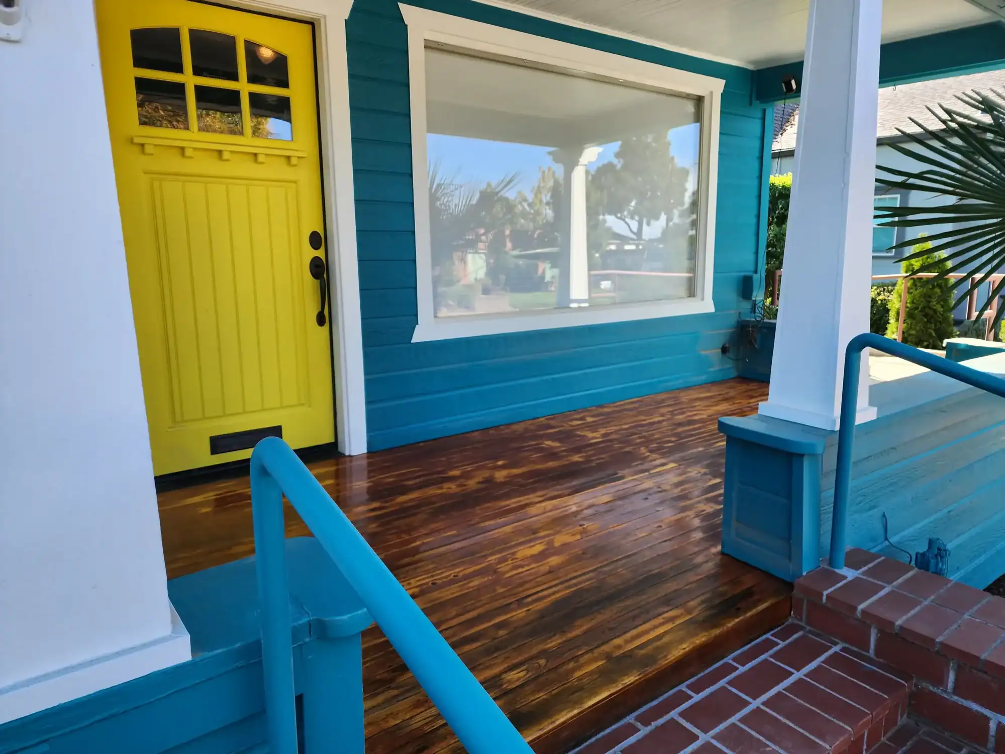 20230928_145923 Teal craftsman bungalow front porch with a bold yellow front door, freshly stained wood deck boards, and teal painted railings