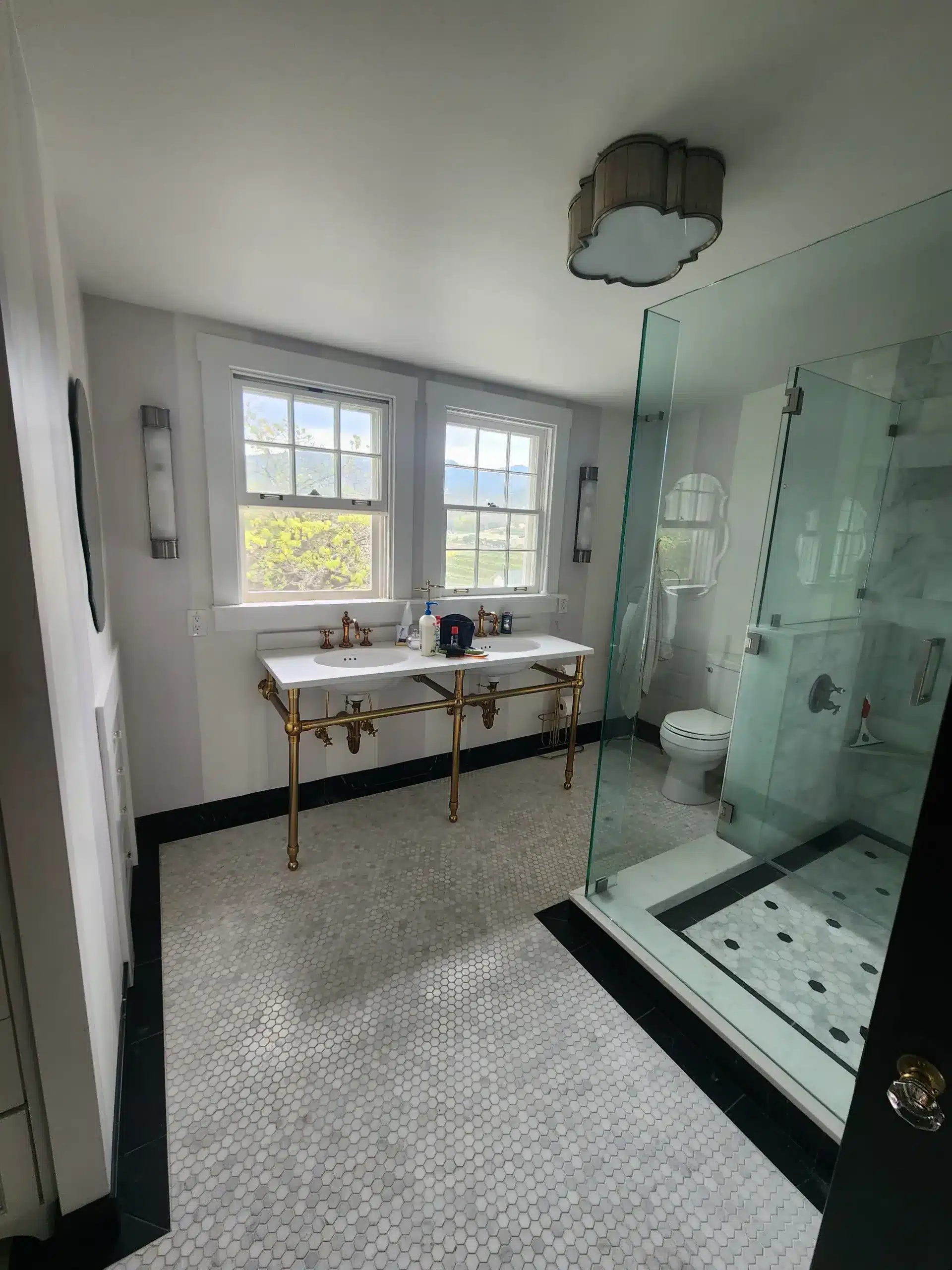 Interior residential painting Freshly painted white bathroom with brass console vanity, penny tile floor, black trim, and glass shower enclosure