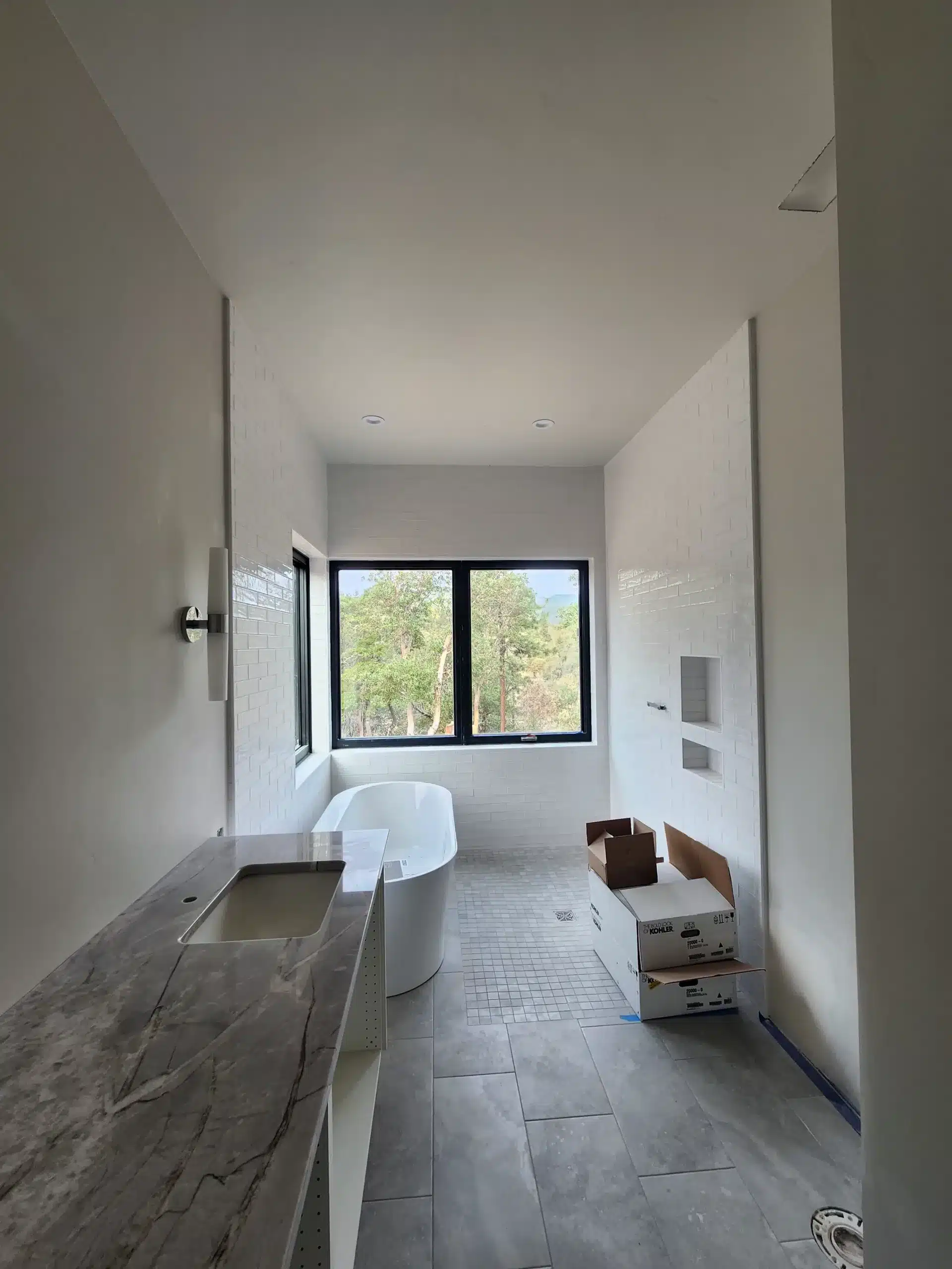 Interior residential painting New construction primary bathroom mid-finish with painted white walls, marble vanity, freestanding tub, and Kohler fixtures still in boxes