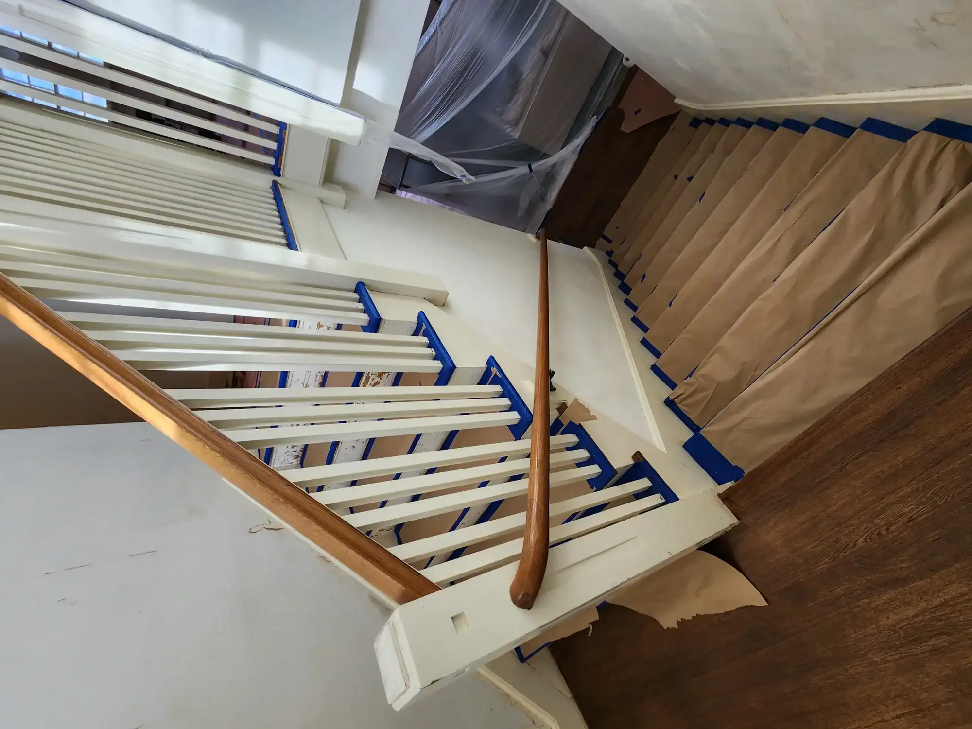 Interior residential painting Staircase balusters taped and freshly painted white with wood treads protected under kraft paper