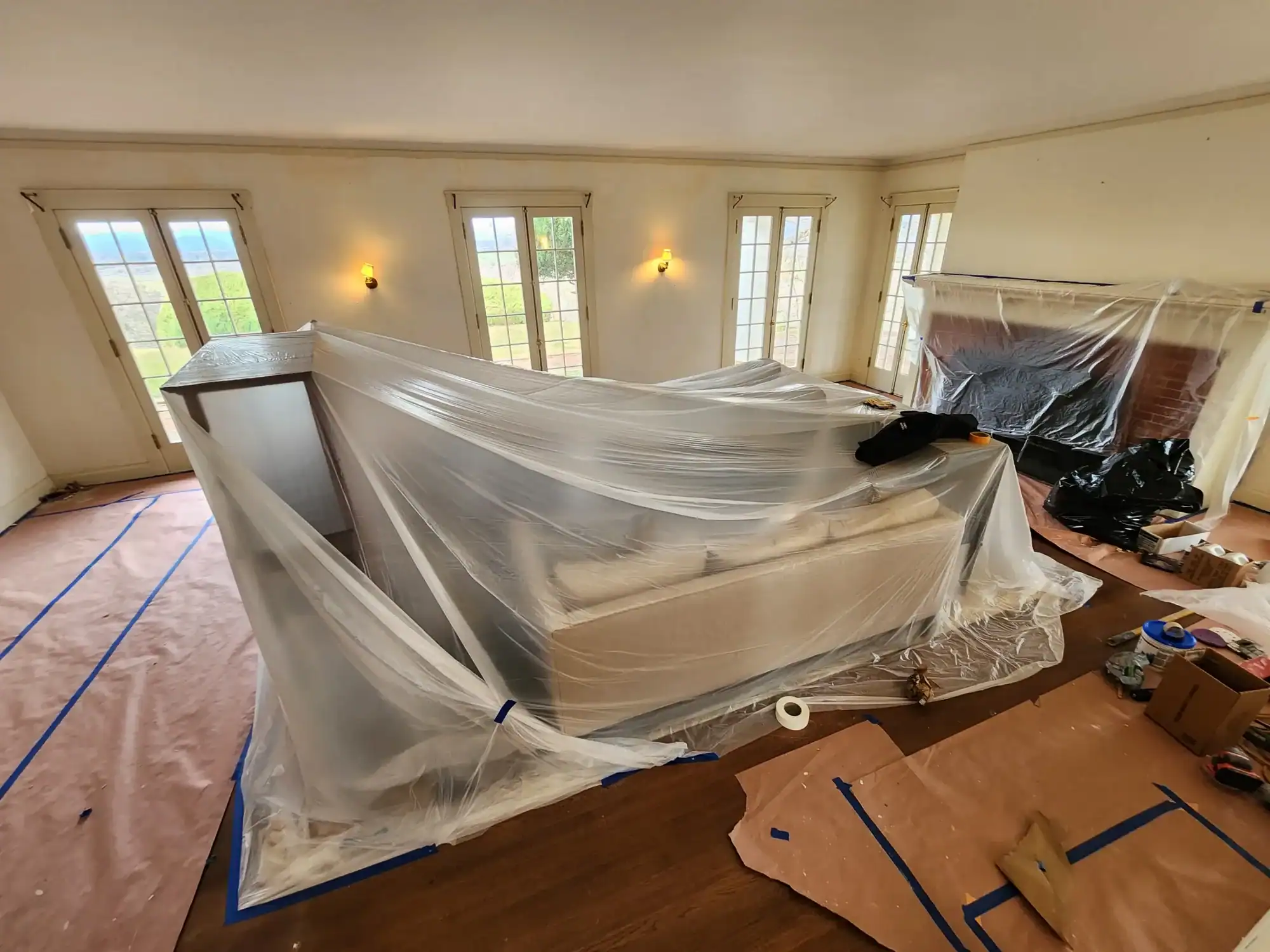Interior residential painting Living room fully prepped for interior painting with furniture, fireplace, and floors protected under plastic sheeting and paper