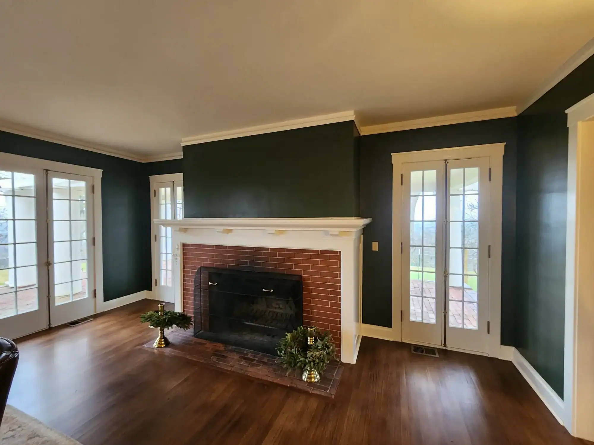 Interior residential painting Freshly painted dark green living room with white crown molding, brick fireplace, and flanking French doors