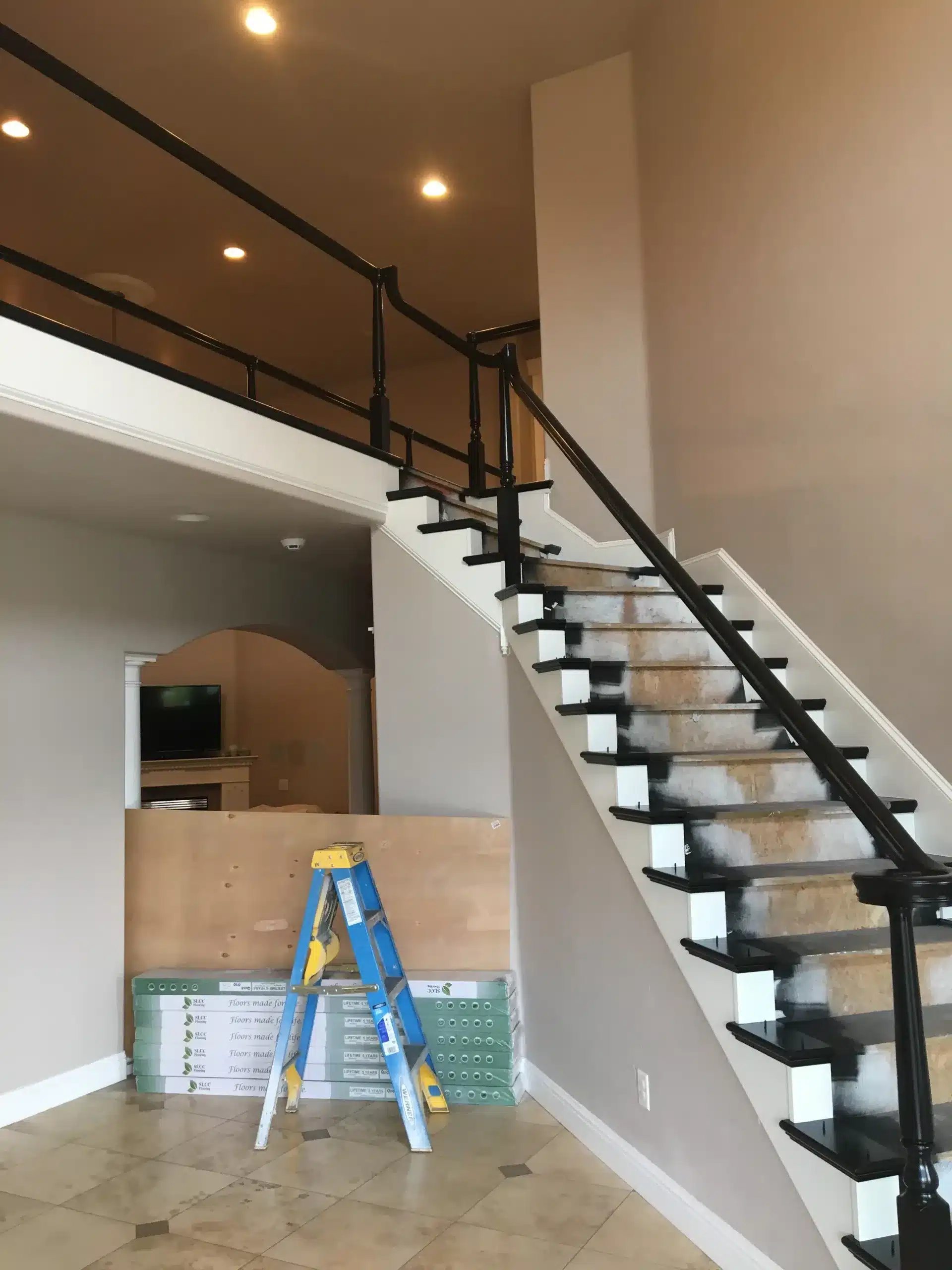 IMG_0688 Two-story foyer staircase with freshly painted black iron railings and white risers, flooring materials staged below mid-renovation