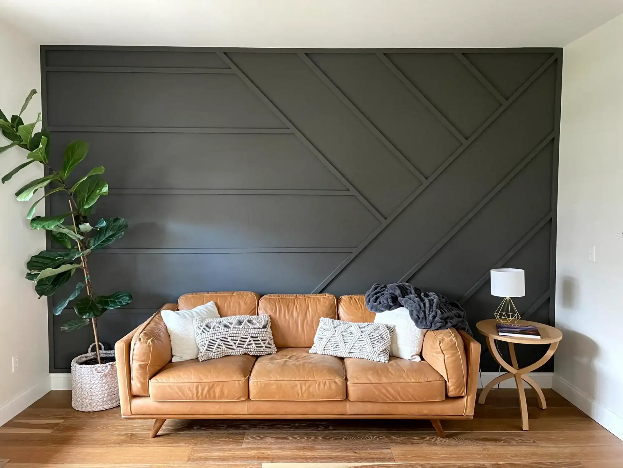 IMG_6370 (1)Interior residential painting Dark charcoal geometric board and batten accent wall behind a tan leather sofa with hardwood floors and a fiddle leaf fig