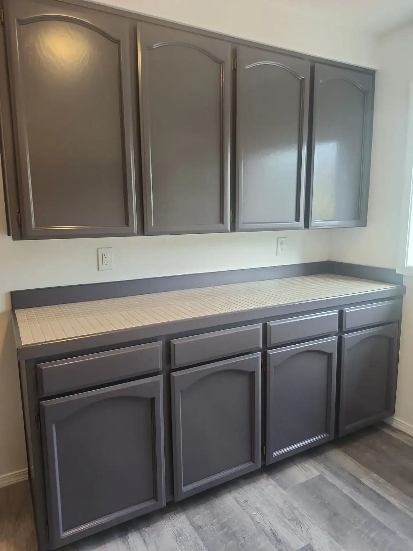 down-net_http20250820-147-kshrmd (1) Arched-panel kitchen cabinets refinished in dark gray over tile countertops and gray laminate flooring