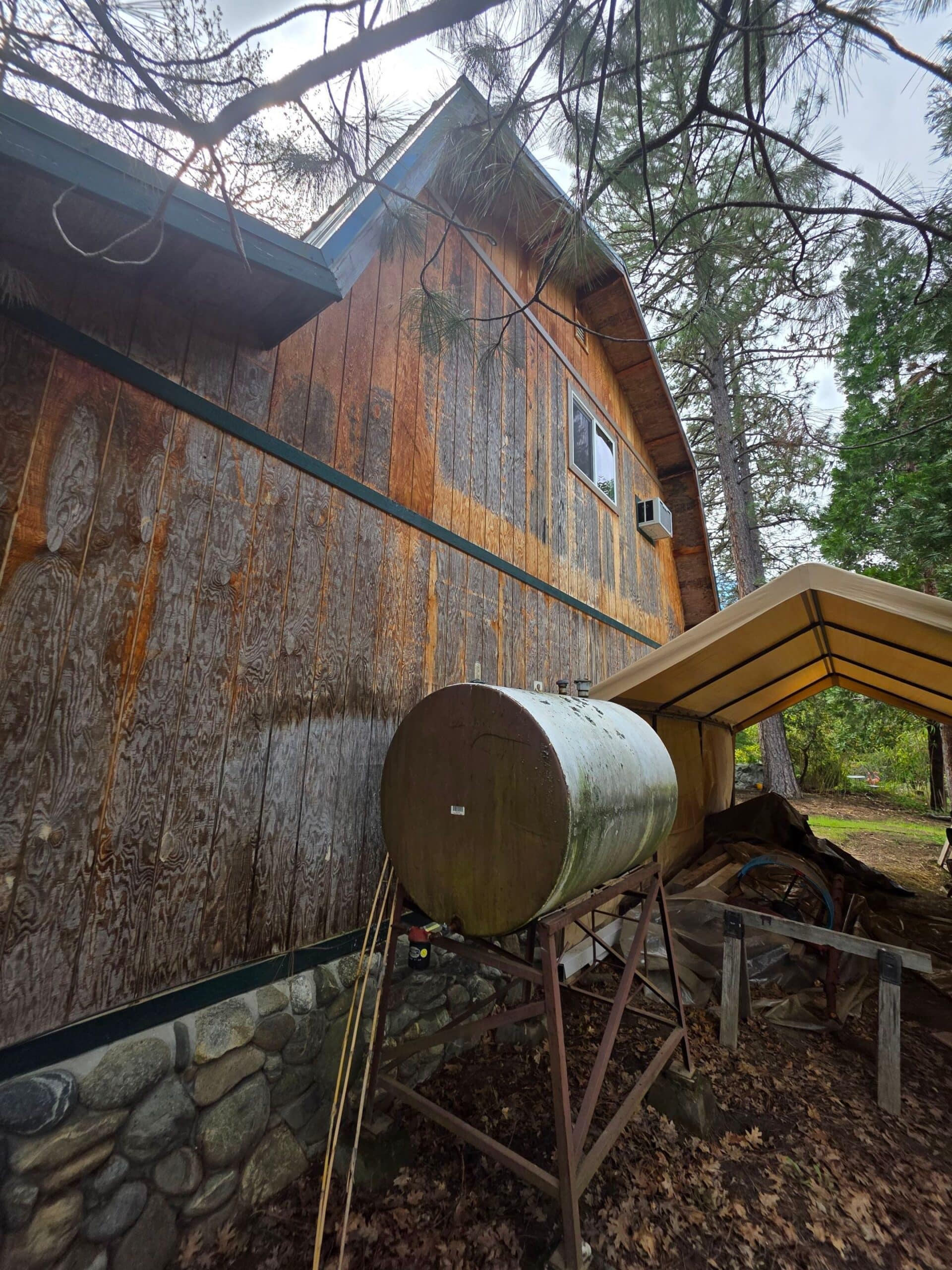 Weathered Wood Cabin Exterior Weathered orange-brown stained wood cabin exterior with dark trim, metal water tank, and stone foundation