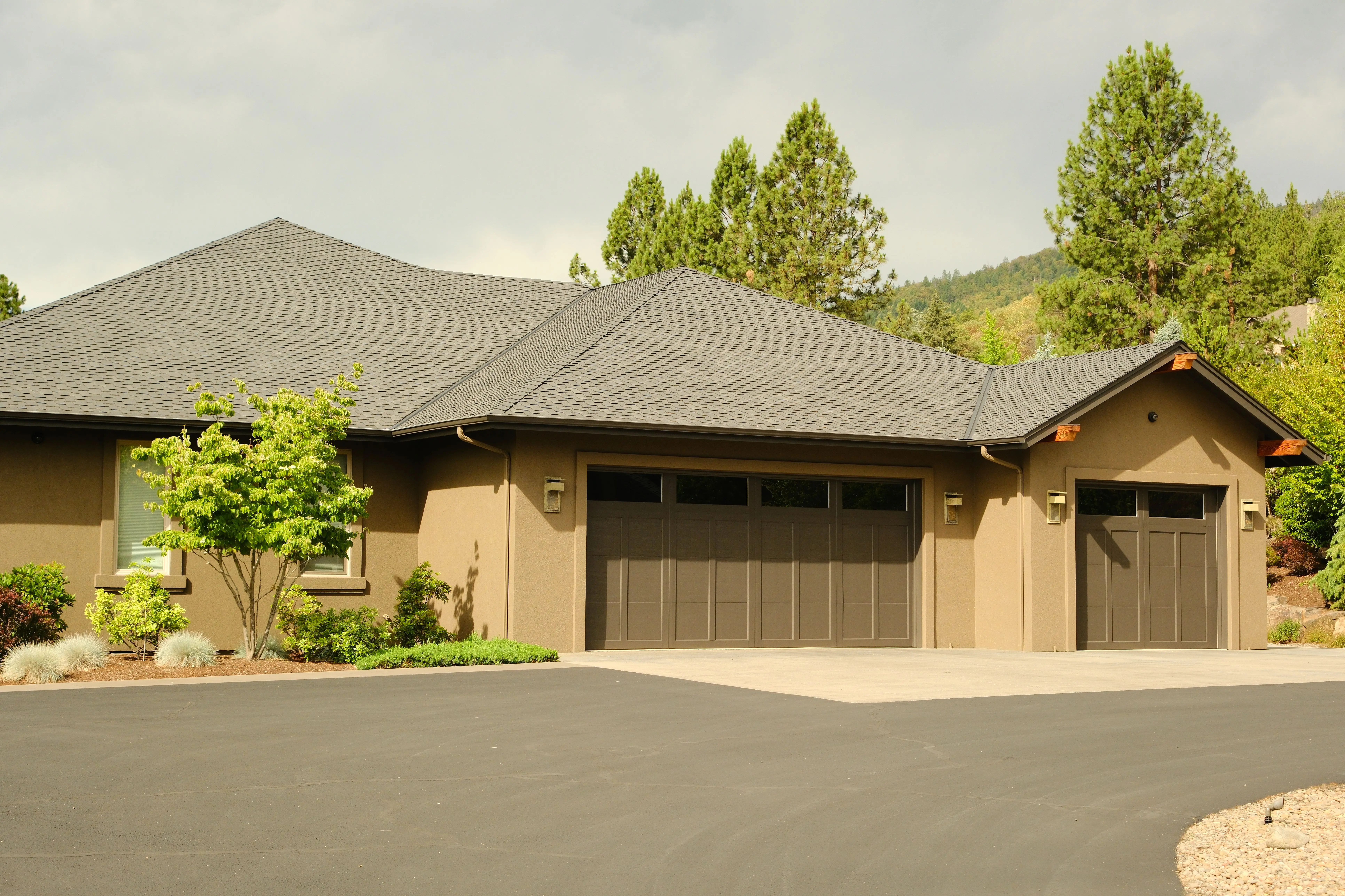 Modern House Exterior Painting Project A large modern residential house with a beautifully painted light brown exterior and dark brown garage doors.